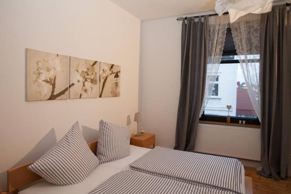 Ein Schlafzimmer mit einem Bett, gestreifte Kissen, einem Nachttisch, einer Lampe und drei Wandbildern.