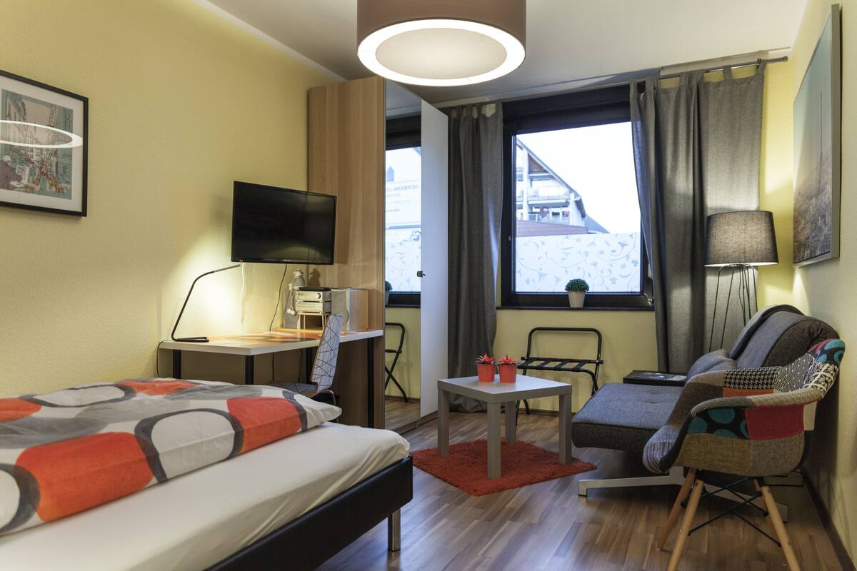 Ein Hotelzimmer mit Bett, Schreibtisch, Stuhl, Fernseher und einem Fenster mit Vorhängen.