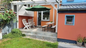 Relax in a serene outdoor space with cushioned chairs and a table, shaded by a green umbrella.