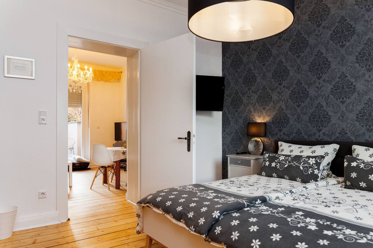 Ein Schlafzimmer mit einem Bett, einem Nachttisch, einer Lampe und einer Wand mit Muster.