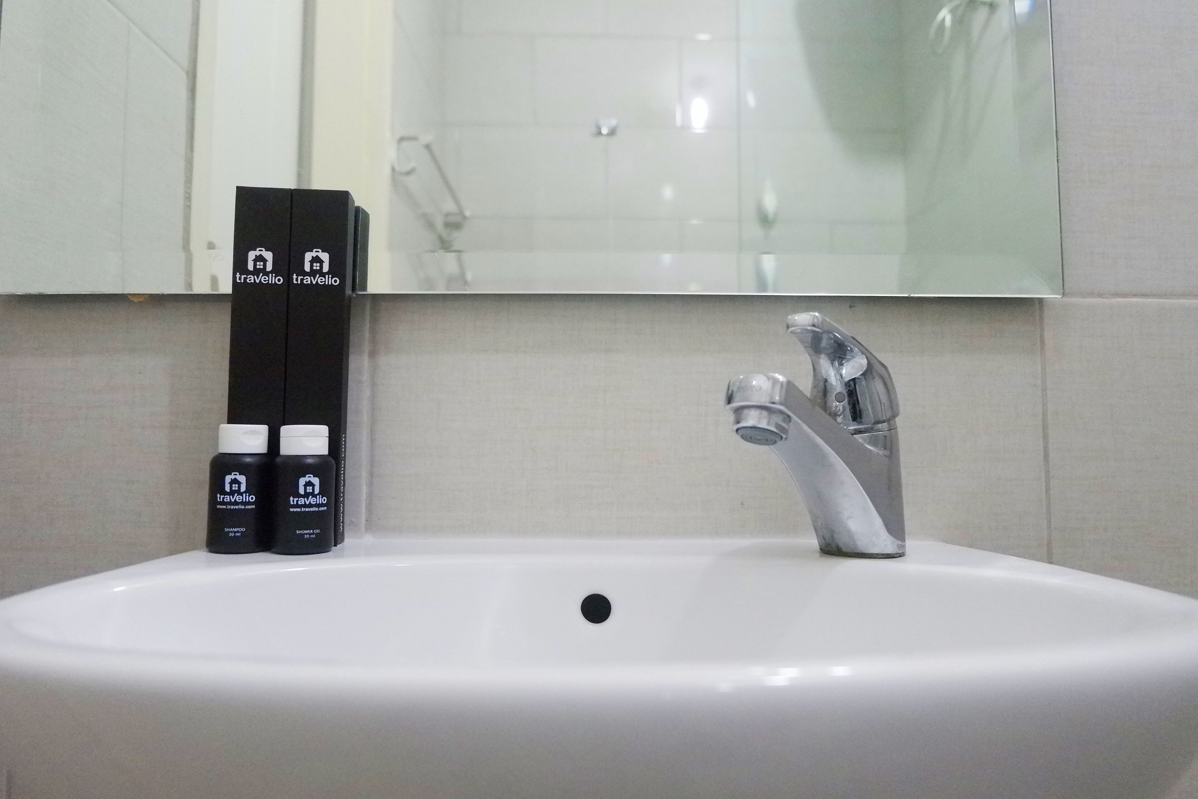 Un baño con un lavamanos blanco, un espejo encima y dos botellas de travelio sobre el borde.