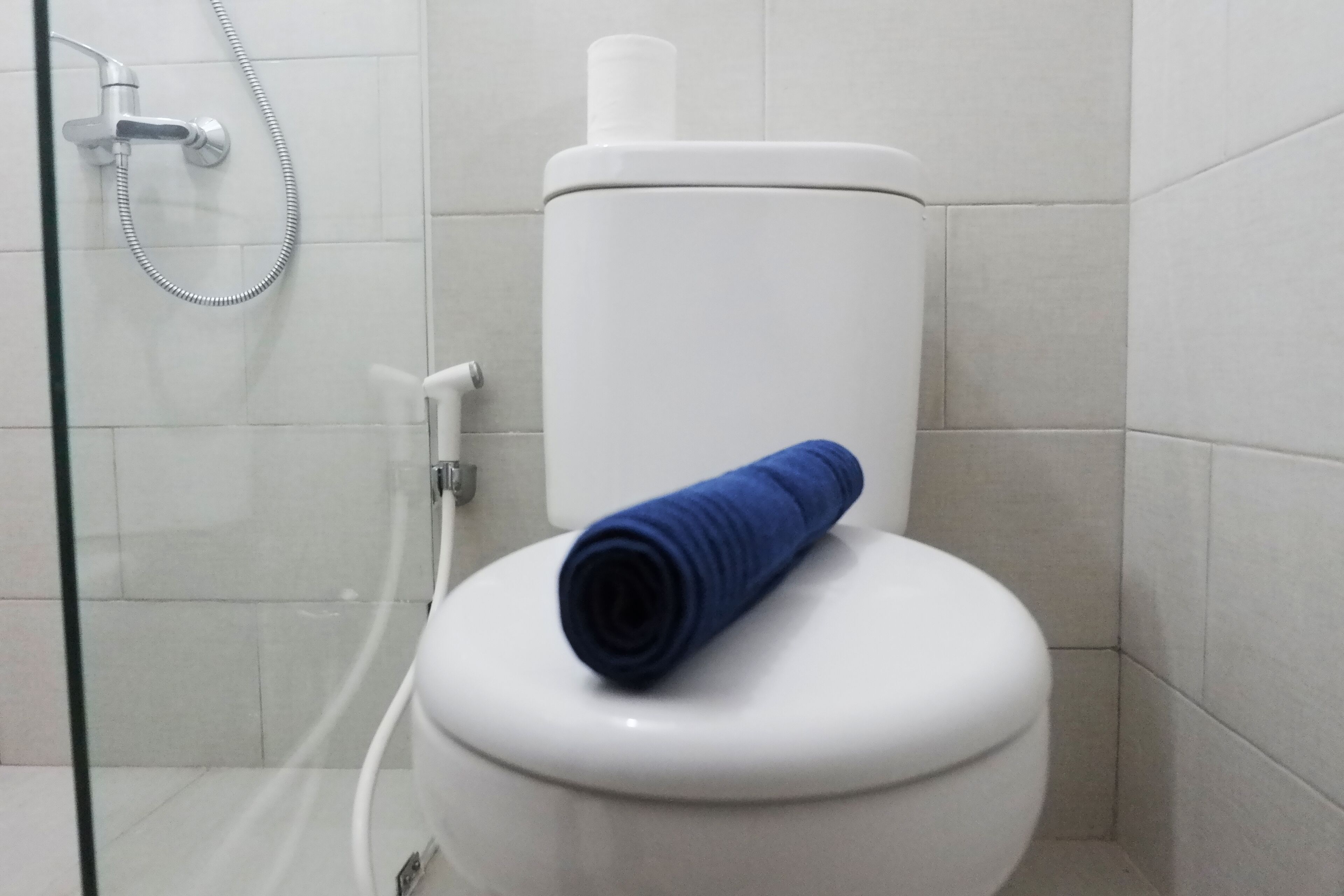 A white toilet with a blue toilet paper holder in a bathroom with white tiles.