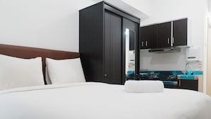 Een hotelkamer met een bed, witte kussens, een donkere kast en een kitchenette met fornuis en gootsteen.