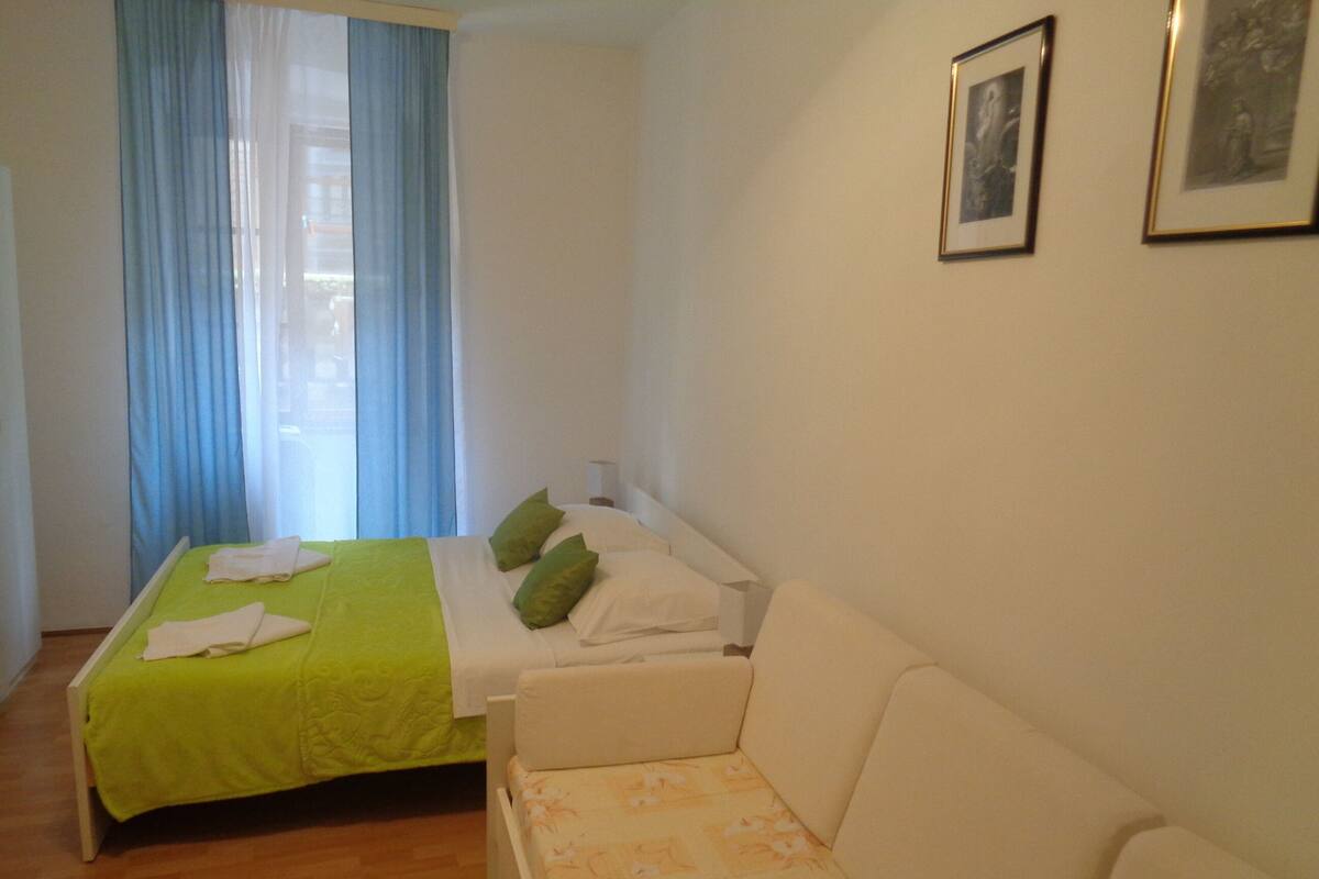 Un dormitorio con cama, sofá, ventana con cortinas azules y dos cuadros en la pared.