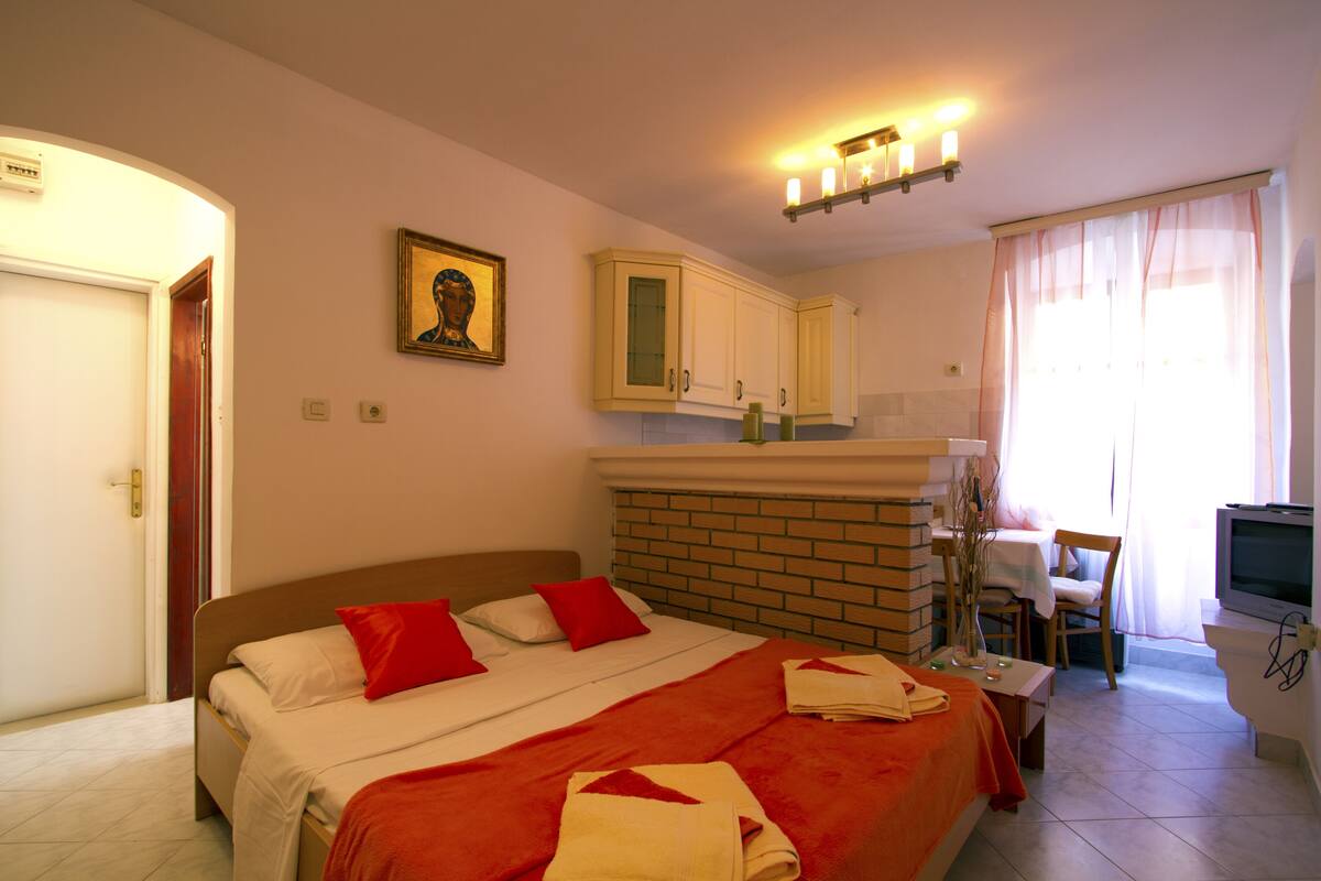 Una habitación de hotel con cama, escritorio con silla, televisión y baño.