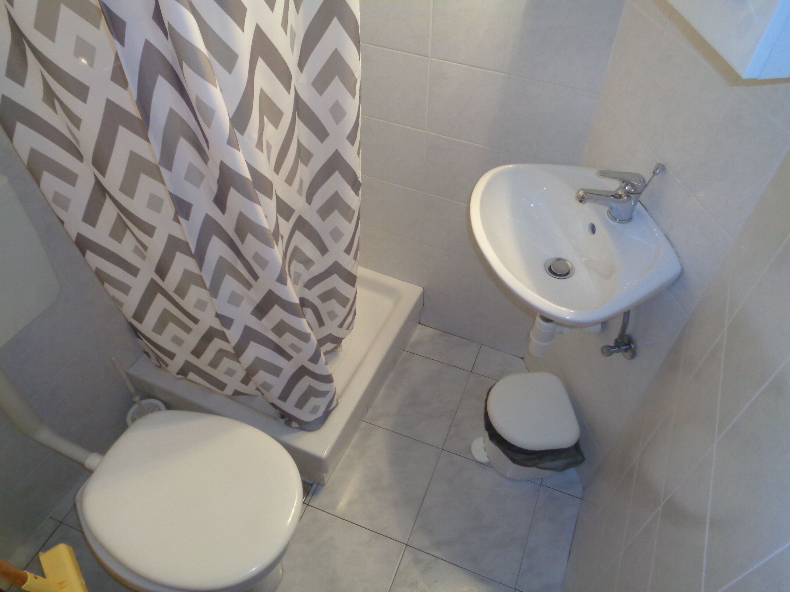 Un baño con inodoro, lavamanos y cortina de ducha con diseño geométrico.