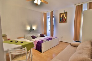 Un dormitorio con cama, escritorio y silla. Hay una ventana con cortinas, un ventilador de techo y una lámpara de pared.