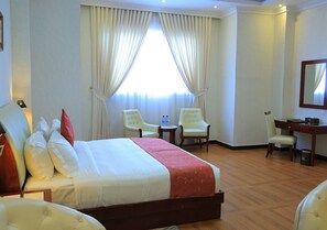 A hotel room with a large bed, two armchairs, a desk, and a mirror. - BON Plaza Hotel Addis Ababa (Addis Ababa)
