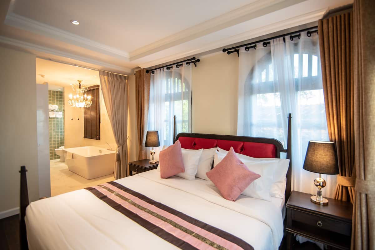 Une chambre d’hôtel avec un grand lit, une salle de bain séparée avec une baignoire et un lustre.