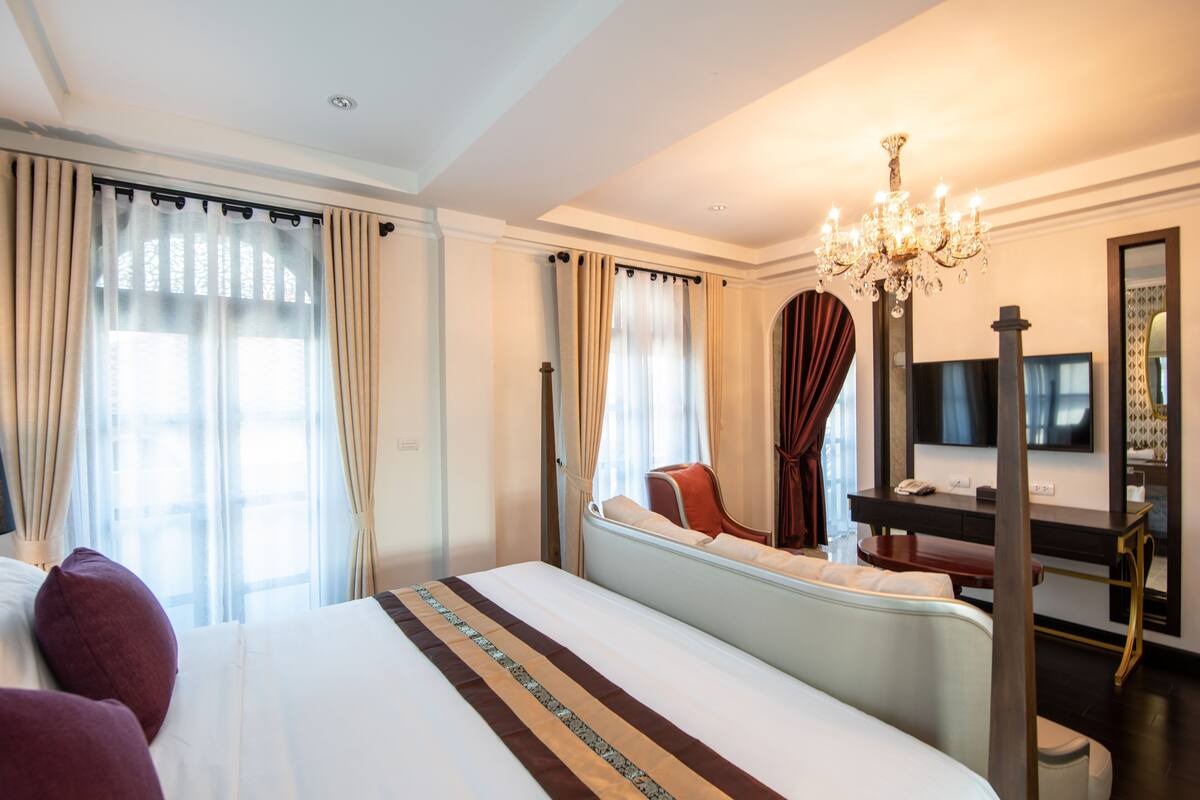 Une chambre d’hôtel avec un grand lit, un bureau, une chaise, une télévision et un lustre.