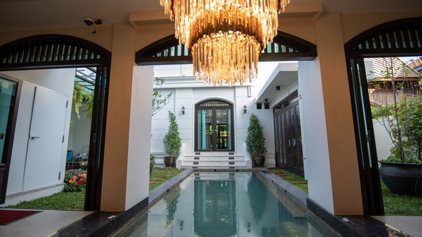 A pool area with a reflective surface, a grand entrance with a double door, and a chandelier above.