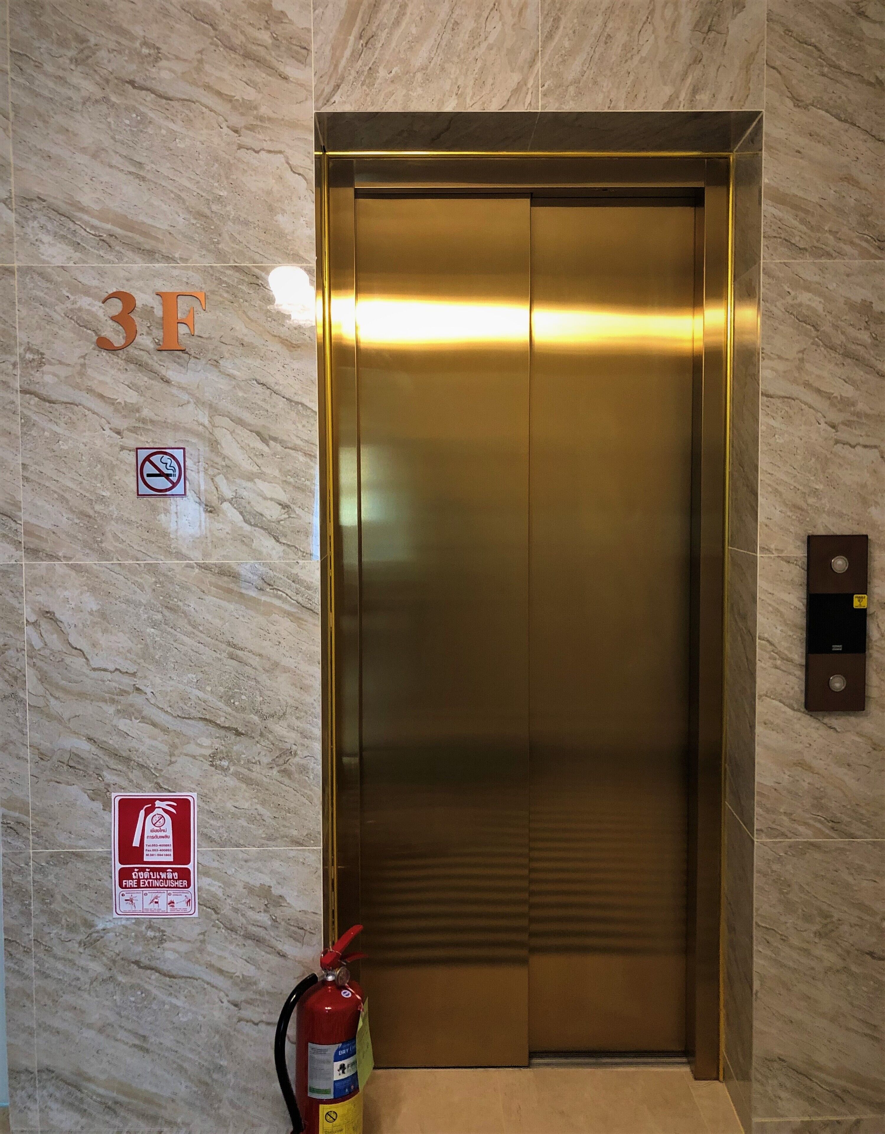 An elevator with a fire extinguisher and a no-smoking sign on the wall.