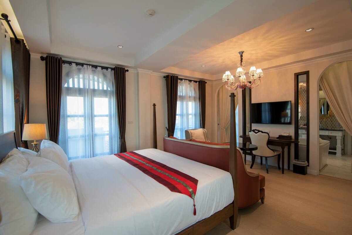 Une chambre d’hôtel avec un grand lit, un bureau, une chaise, une télévision et un lustre.