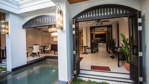A pool area with a glass enclosure, a dining area with chairs and a table, and a kitchen visible through an open doorway.