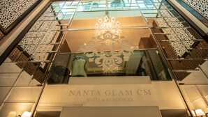 A hotel entrance with a chandelier, glass railings, and a sign reading "NANTA GLAM CM HOTEL & RESIDENCES".
