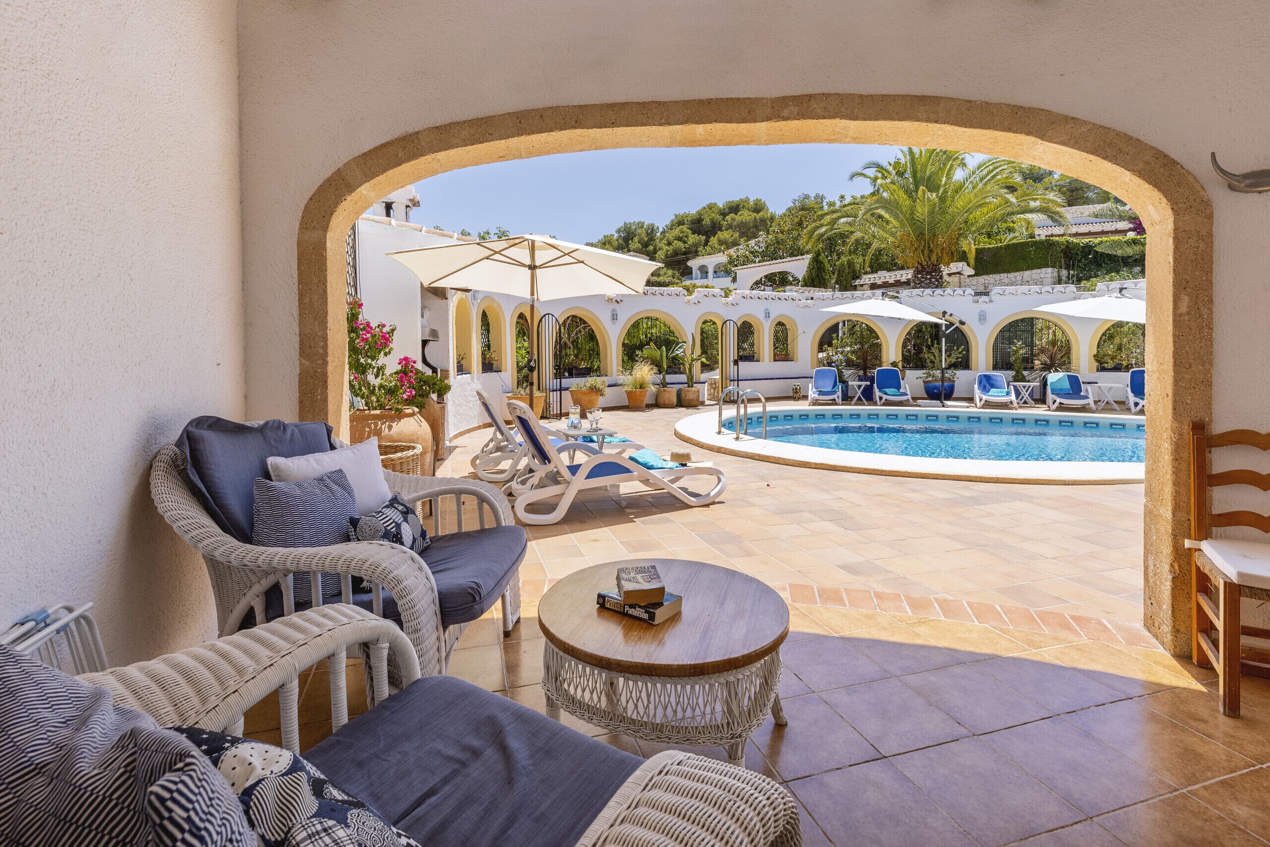 A poolside area with lounge chairs, a small table, and a view of the pool and surrounding greenery.