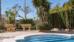 A swimming pool with a curved edge, surrounded by stone benches and lush greenery. - Atico Salonica (Javea / Xàbia)