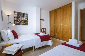 Ein Hotelzimmer mit zwei Betten, einem großen Holzschrank, einem Poster an der Wand und einem Nachttisch mit einem Buch und einem Glas Orangensaft.