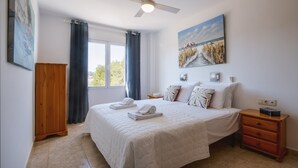 A bedroom with a bed, a nightstand, a wooden wardrobe, a ceiling fan, and a window with curtains. - Atico Salonica (Javea / Xàbia)
