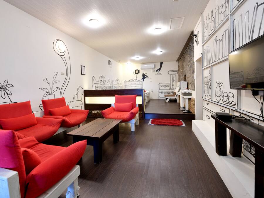 A hotel room with a sofa set, a wooden table, a TV, and a wall with decorative drawings.