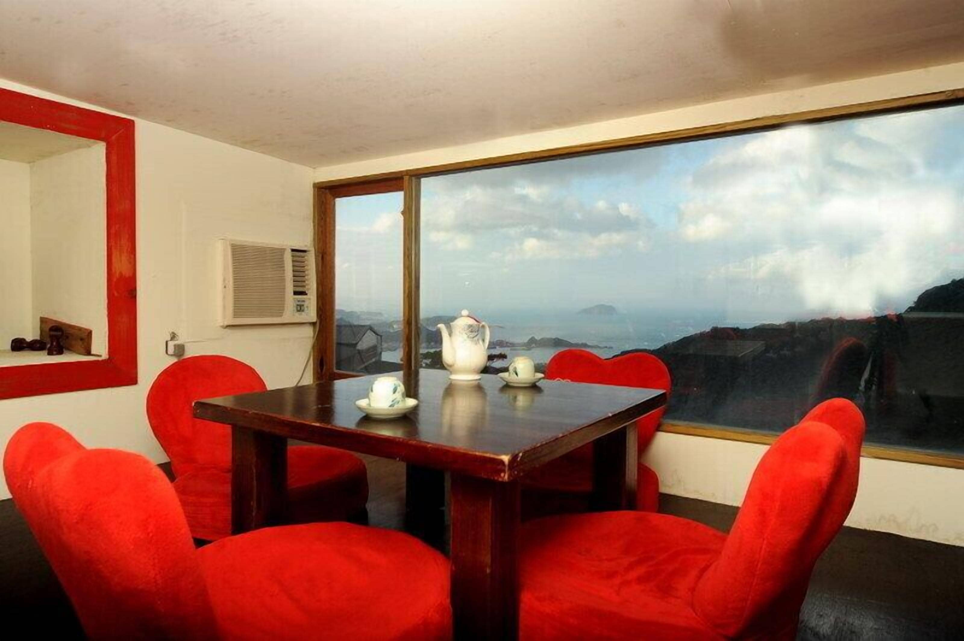 A room with a large window, a wooden table, and red chairs.