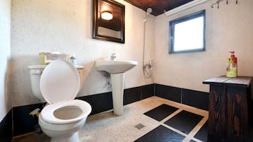 A bathroom with a toilet, sink, shower, and a window.