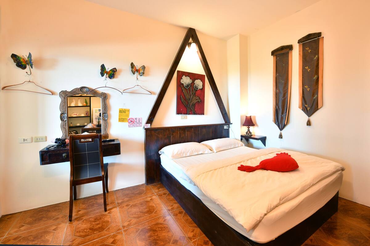 A bedroom with a bed, a desk, a chair, a dresser, a mirror, and wall decorations including butterflies and a painting.