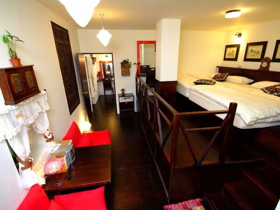 A compact hotel room with a bed, a small table, and a chair. There is a staircase leading to an upper level.