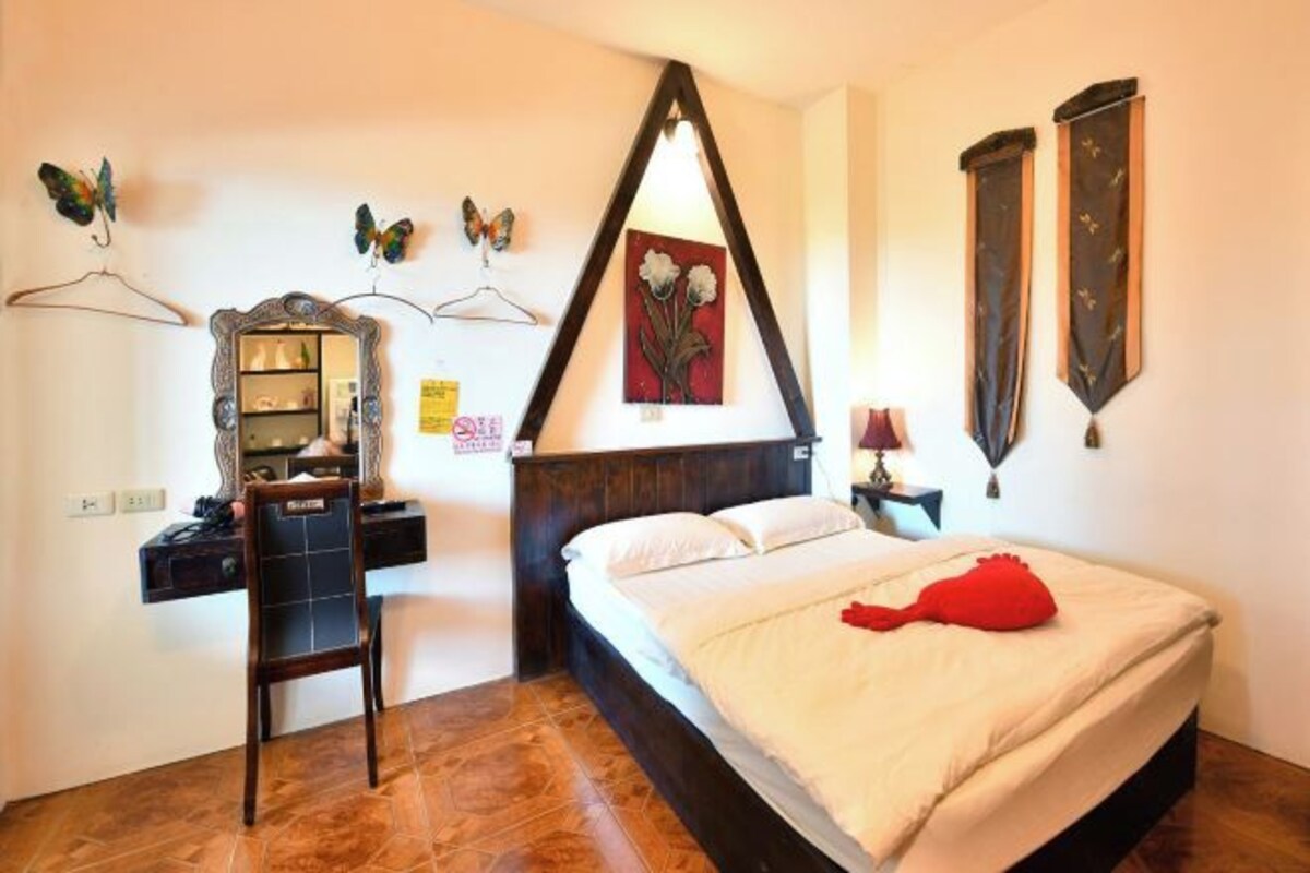 A bedroom with a bed, a desk with a chair, a dresser, a mirror, and wall decorations including butterflies and a painting.