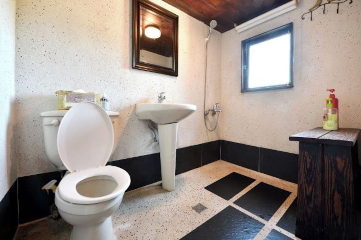 A bathroom with a toilet, sink, shower, and a small window.