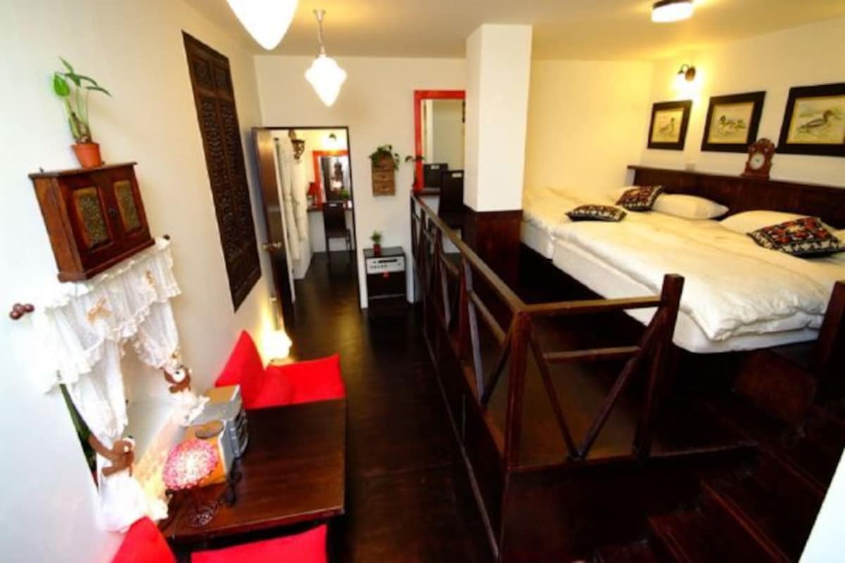 A room with a bed, a desk, and a chair. There is a mirror, a plant, and a picture on the wall.