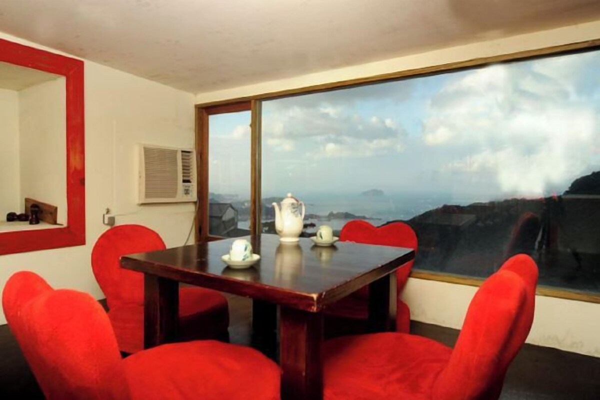 A room with a large window, a wooden table, and red chairs.