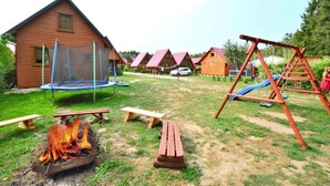 Una cabaña de madera con un trampolín, un conjunto de columpios y un hogar en el patio.