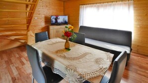 Una cabaña acogedora con interior de madera, una mesa de comedor con mantel de encaje, un sofá y un televisor sobre un mueble.