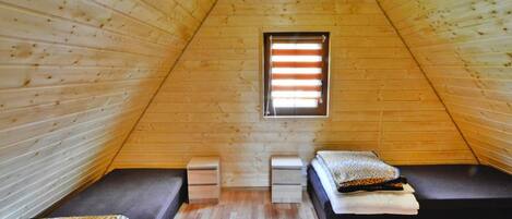 Una habitación pequeña de madera con forma triangular, dos camas, una ventana y una mesita.