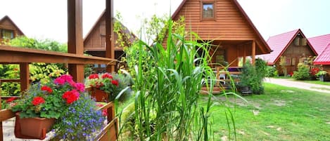 A wooden cabin with a porch, surrounded by a well-maintained garden with various plants and flowers.