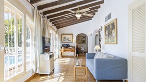 A spacious living area with a blue sofa, a wooden coffee table, and a ceiling fan. There is a kitchen area in the background with a dining table and chairs. - Villa Levante (Javea / Xàbia)