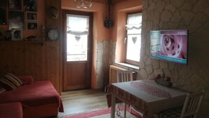 A cozy room with a wooden interior, a dining table with chairs, a red sofa, and a television mounted on the wall. - Relaxation & Skiing in the Heart of the Dolomites UNESCO (Calalzo di Cadore)