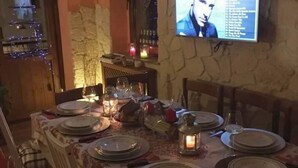A dining table set with plates, glasses, and candles, with a television mounted on the wall displaying a list. - Relaxation & Skiing in the Heart of the Dolomites UNESCO (Calalzo di Cadore)