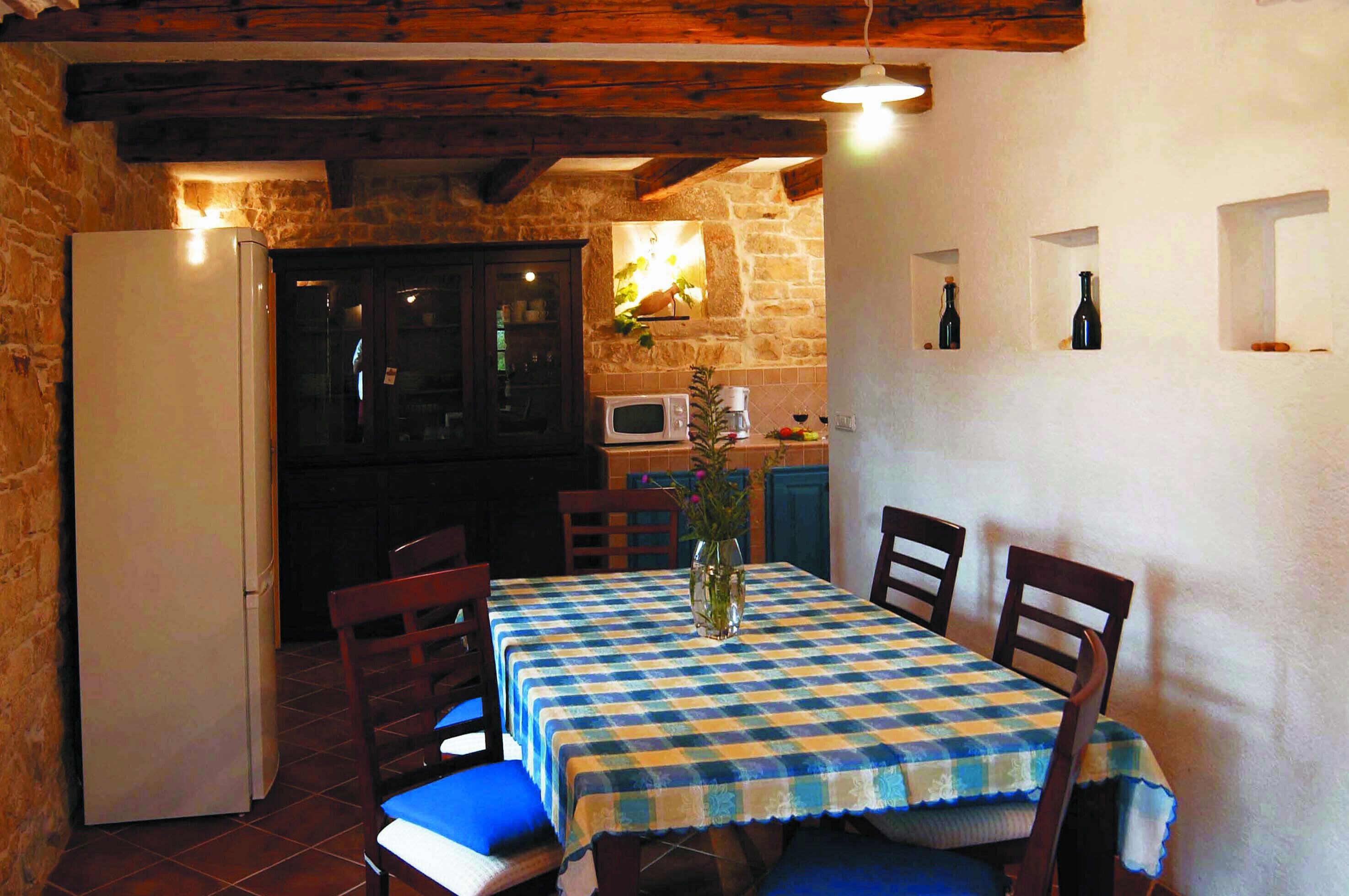 A dining area with a checkered tablecloth, wooden chairs, a vase with flowers, and a stone wall.