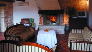 A cozy room with a fireplace, striped sofas, a round table with a fruit bowl, and a television on a wooden cabinet. - Marvelous Istrian Villa Morus (Svetvincenat)
