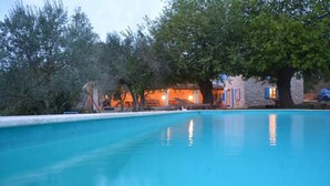 A clear blue swimming pool surrounded by trees and a stone building with a warm light. - Marvelous Istrian Villa Morus (Svetvincenat)