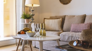 A cozy living room with a sofa, a small round table with a lamp, a bowl of fruit, and two bottles of champagne. - Golden Beach (Javea / Xàbia)