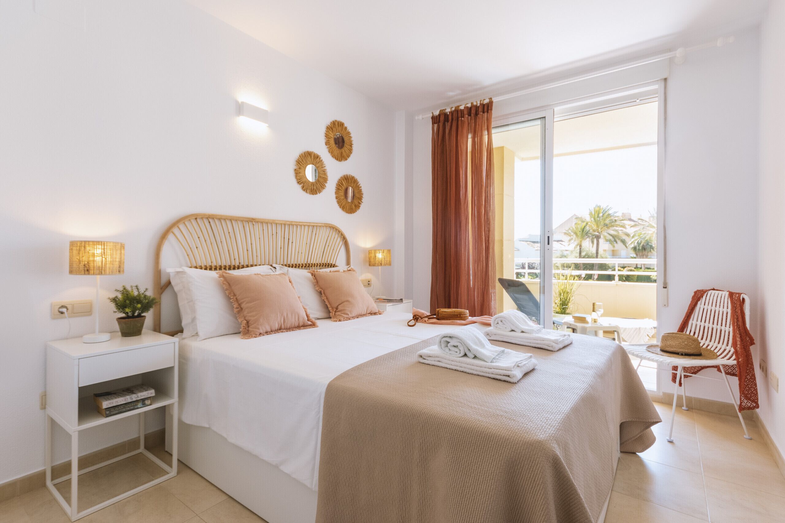 A hotel room with a bed, bedside tables, a chair, a balcony with a view, and a window with curtains.