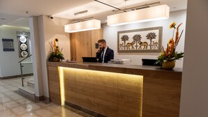 A reception desk with a wooden finish and a modern design, featuring a digital screen and a vase with flowers. - Ambassador Boutique Hotel (Jerusalem)