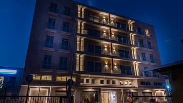 Un hotel de varios pisos con diseño moderno, que cuenta con balcones en cada planta, ventanas iluminadas y una entrada bien iluminada.