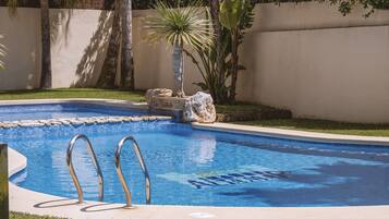 A swimming pool with clear blue water, a ladder, and a small rock feature.