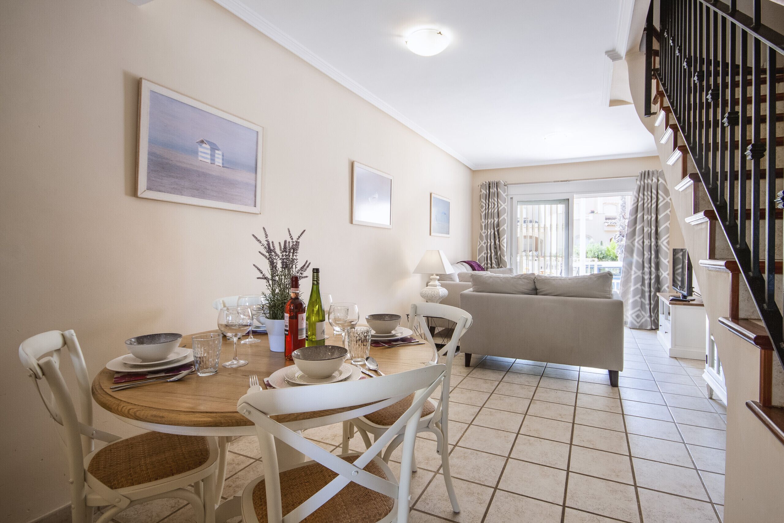 A dining area with a wooden table, white chairs, and a sofa in the background.