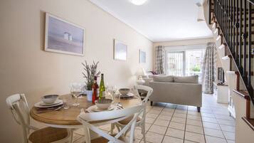 A dining area with a wooden table, white chairs, and a sofa in the background.