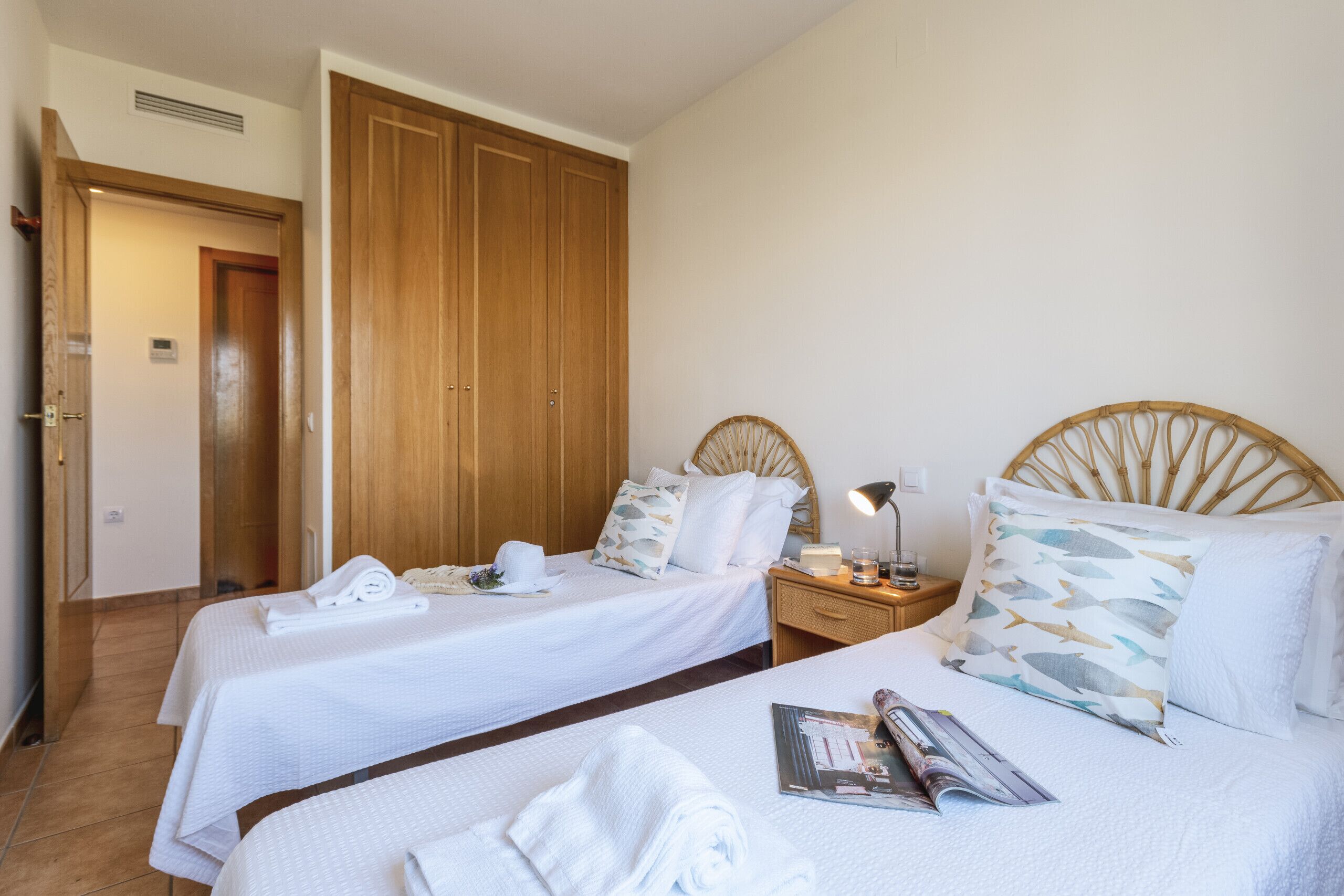 Habitación de hotel con dos camas, un armario de madera y una mesita de noche con lámpara.